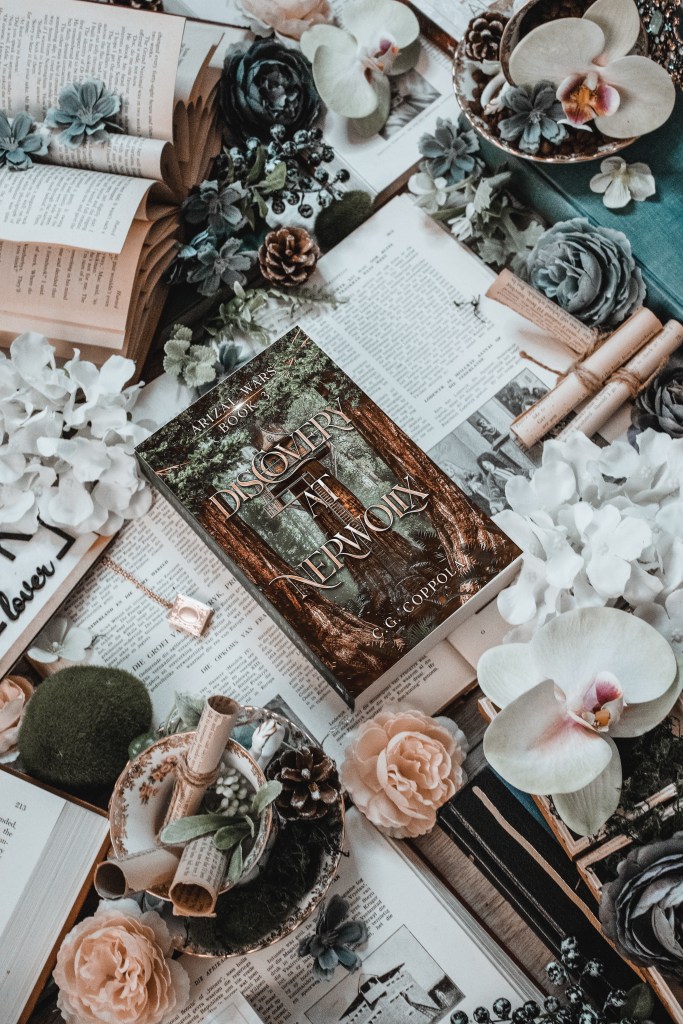 Flatlay photo of Discovery at Nerwolix by C.G. Coppola, styled among vintage books, orchids, pinecones, and scrolls. The forest-green fantasy cover features towering trees and an ancient wooden doorway glowing with mystery.